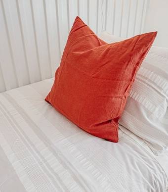 Pormenor de uma almofada laranja em cima de uma cama de solteiro